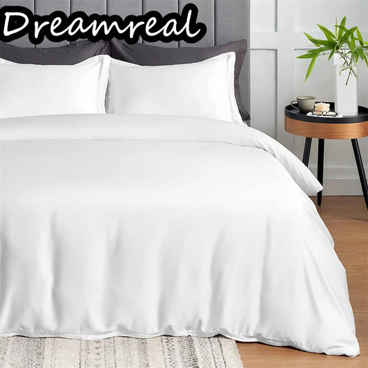 White bedding set on a bed with 'Dreamreal' branding, side table with decor items in the background.