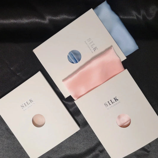 Silk scarves in pink and blue on a black satin background with 'SILK' branding.