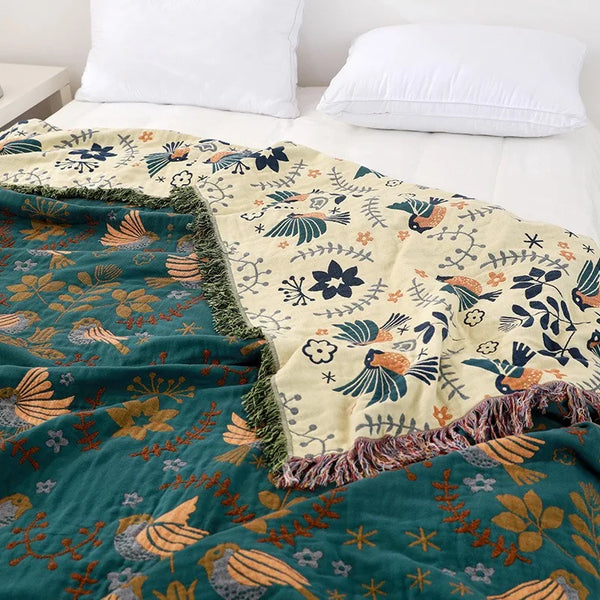 Floral and bird patterned blanket draped over a bed with white pillows.