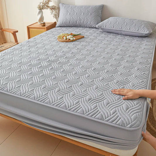 Gray quilted mattress cover on a bed with a hand touching it, in a bedroom setting.