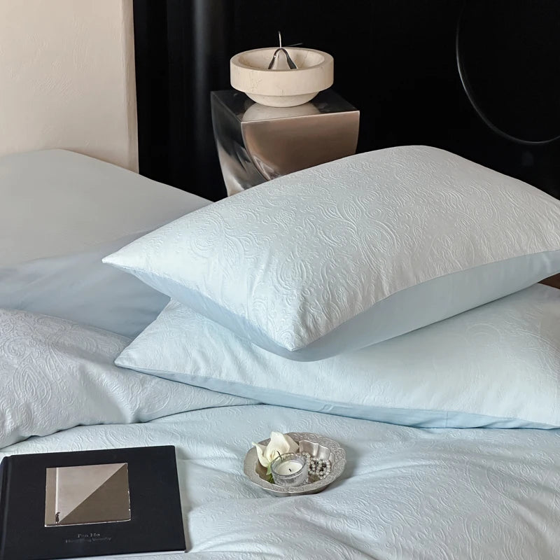 Light blue bedding set with decorative pillows on a bed.