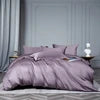 Purple bedding set on a bed with a white pillow and bottle in the background.