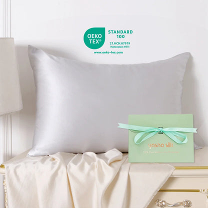 White pillow on a bed with a green box featuring 'Yasha Silk' branding, OEKO-TEX certification visible.