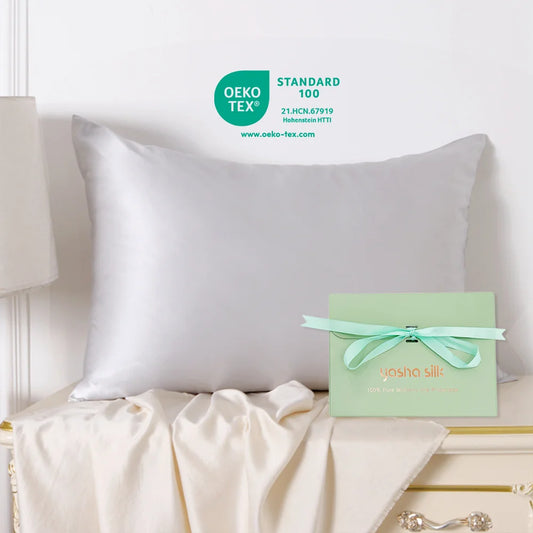 White pillow on a bed with a green box featuring 'Yasha Silk' branding, OEKO-TEX certification visible.
