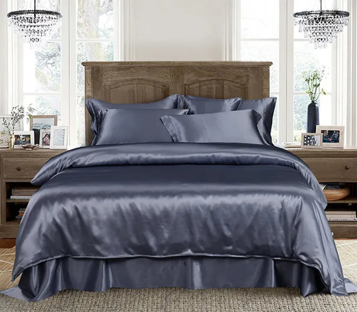 Gray satin bedding set on a bed in a well-lit bedroom with wooden headboard and nightstands.