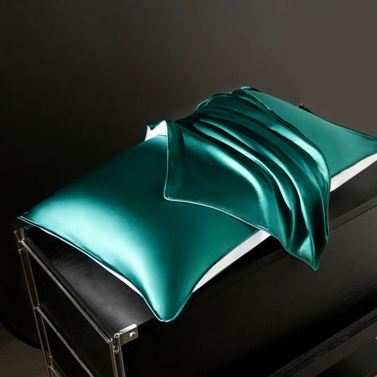 Teal satin pillowcase on a black surface with a dark background