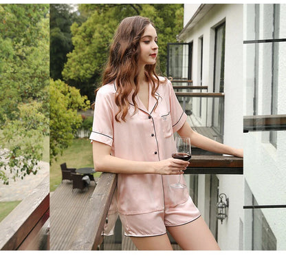 Woman in pink satin pajama set holding a glass of red wine on a balcony.