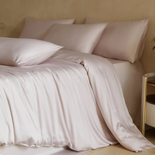 Neatly made bed with light pink bedding and pillows against a beige wall.