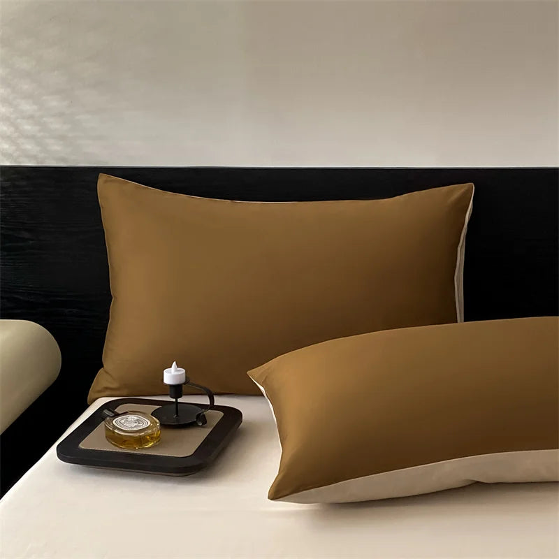 Two brown pillows on a bed with a small tray and candle in the foreground.