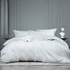 White comforter on a bed with a gray wall in the background