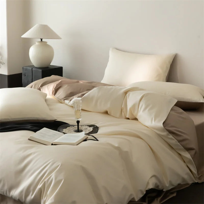 Neatly made bed with beige bedding, a lamp on a nightstand, and an open book with a glass of wine.