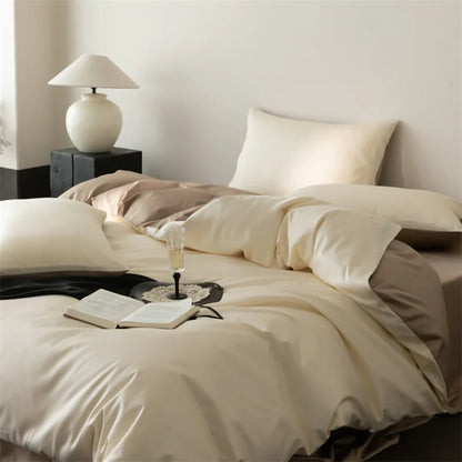 Neatly made bed with beige bedding, a lamp on a nightstand, and an open book with a glass of wine.