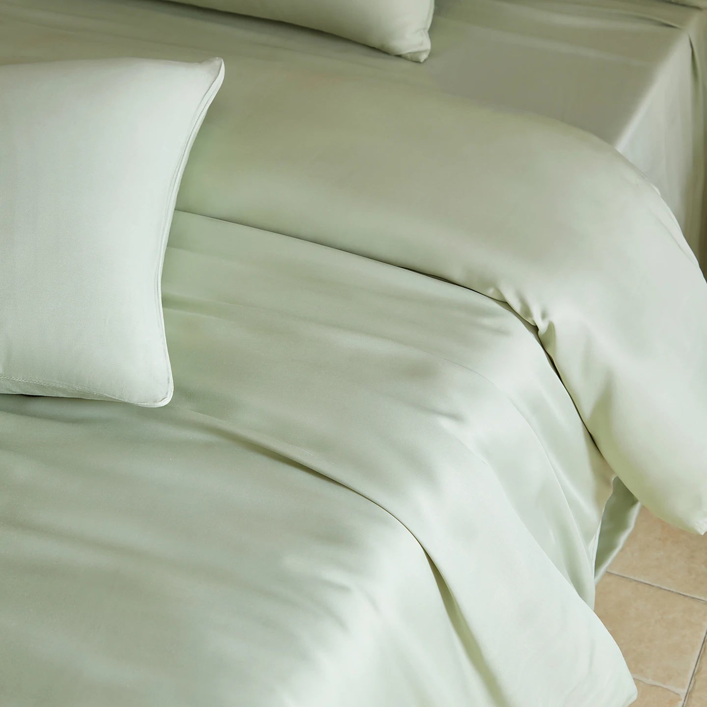 Green satin sheet set on a bed with white pillows.