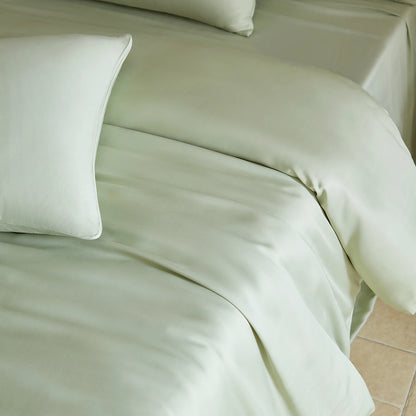Green satin sheet set on a bed with white pillows.
