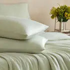 Neatly made bed with white bedding and pillows, featuring a vase of yellow flowers on a side table.