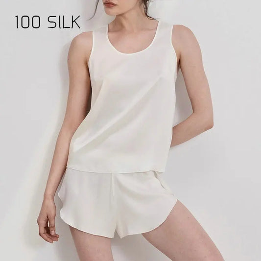 Woman wearing a white silk tank top and shorts set on a plain background with '100 SILK' text.