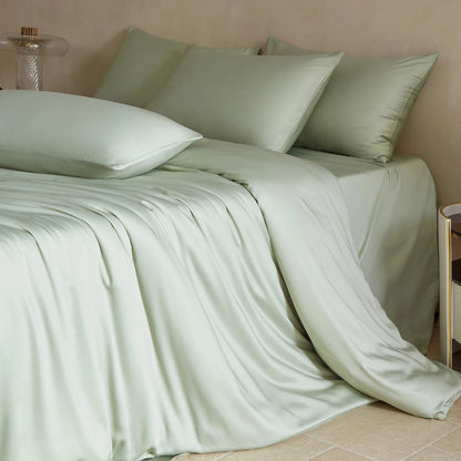 Light green bedding set on a bed with pillows against a beige wall.