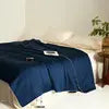 Navy blue bedspread on a bed with a white wall and plant in the background