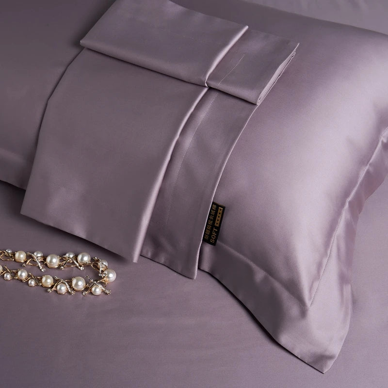 Purple satin pillowcases on a matching purple fabric with a necklace beside them.