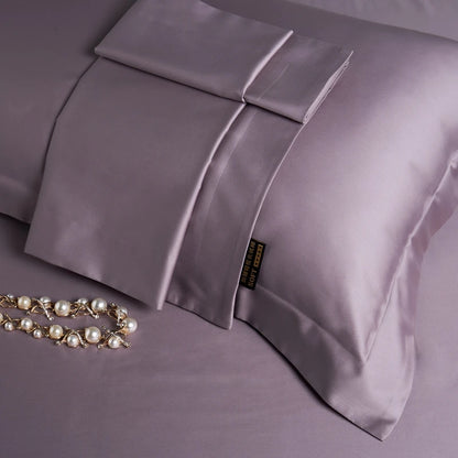 Purple satin pillowcases on a matching purple fabric with a necklace beside them.