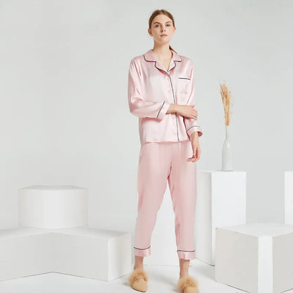 Woman wearing a pink satin pajama set in a minimal white room.