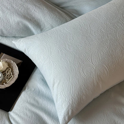 White textured pillow on a light blue bedspread with a decorative plate in the corner.