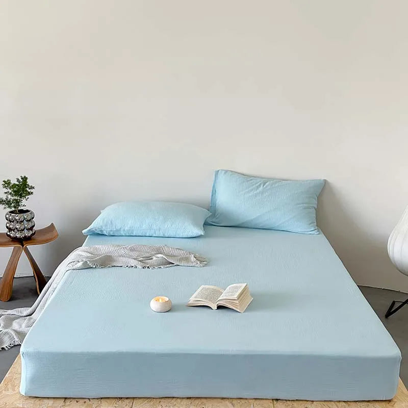 Light blue bedspread on a bed with a candle and book, in a minimalistic room.