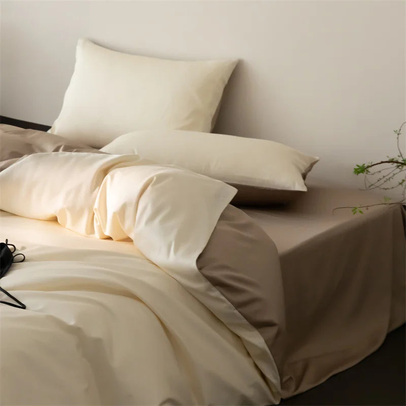Neatly made bed with beige bedding and pillows against a plain wall.