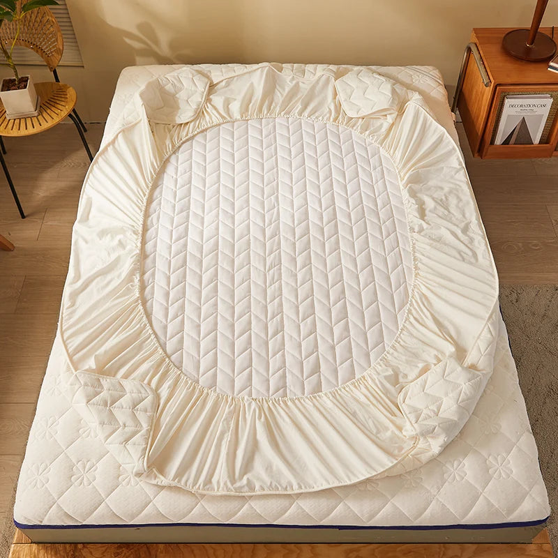 Quilted mattress cover on a bed in a room with a wooden side table and plant.