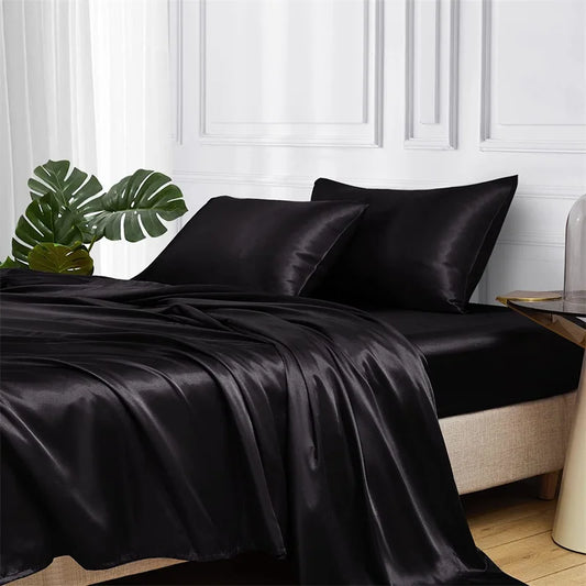Black satin bedding set on a bed with a white wall and plant in the background