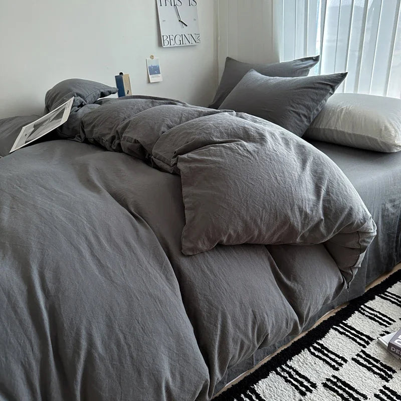 Gray bedding set on a bed with a window and decor in the background