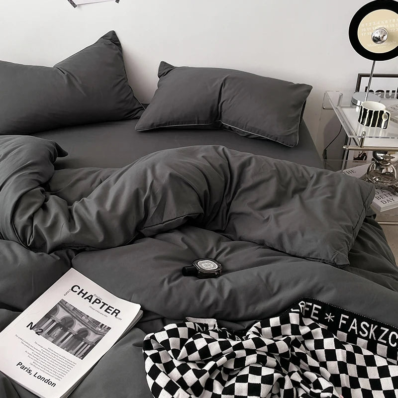 Gray bedding set on a bed with a magazine and checkered blanket.