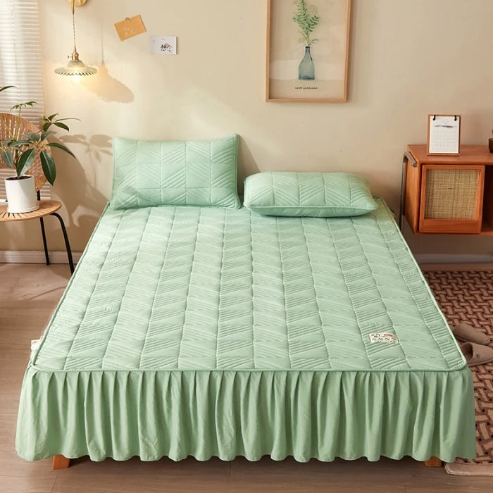 Green quilted mattress cover on a bed in a room with a side table and plant.