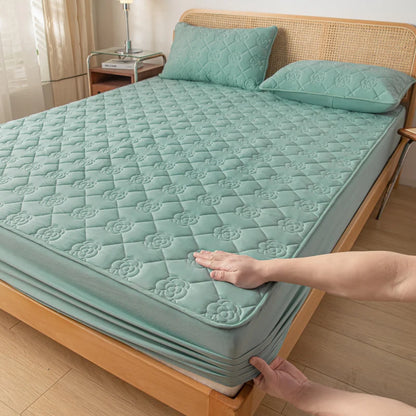 Person adjusting a green quilted mattress cover on a bed.