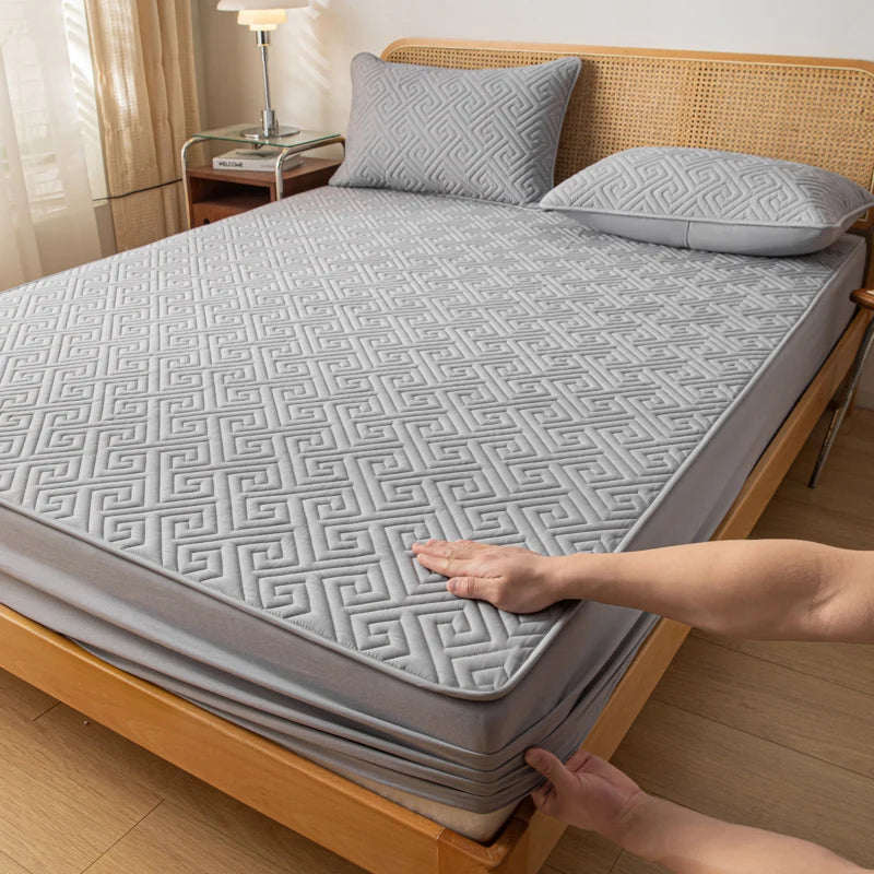 Person adjusting a gray mattress cover on a wooden bed in a bedroom.