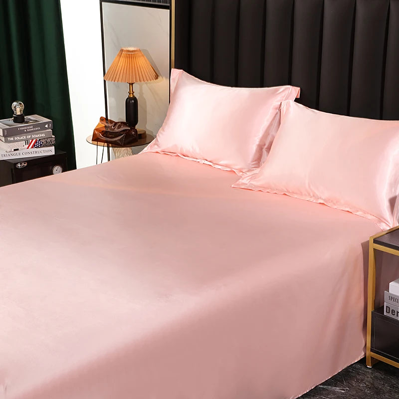 Pink satin bedding set on a bed with a lamp and books in the background.