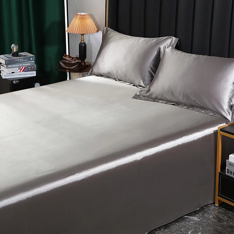 Gray satin sheet set on a bed with a lamp and books in the background.