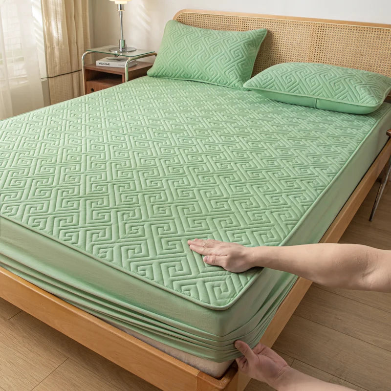 Green quilted mattress cover being adjusted on a wooden bed in a bedroom.