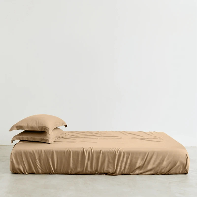 Beige bedspread and pillows on a bed against a plain background