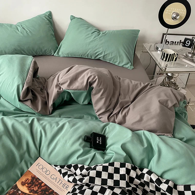 Mint green bedding set with gray comforter on a bed, next to a nightstand with a clock.