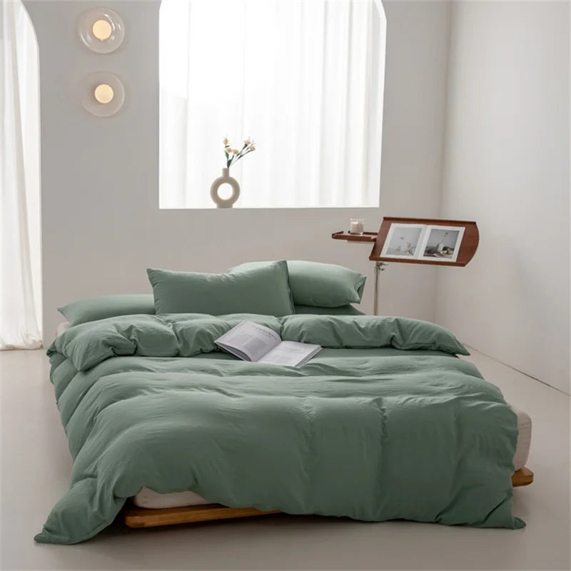 Green bedspread on a bed in a minimalistic room with a window and side table.