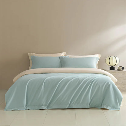 Light blue bedding set with beige comforter on a bed in a room with a lamp and nightstand.
