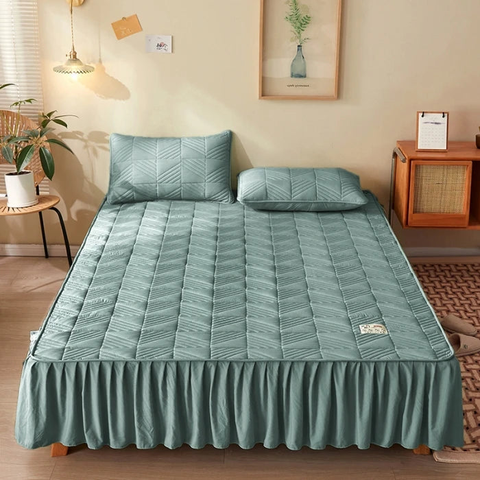 Green quilted mattress cover on a bed in a room with a lamp and plant.