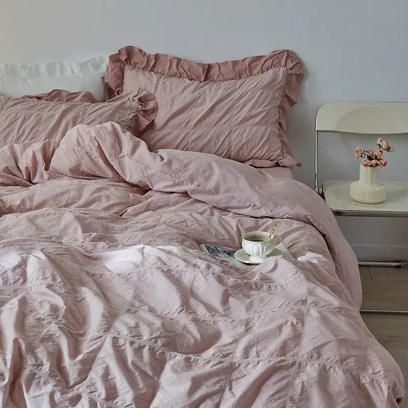 Pink bedding with a cup and saucer on a bed in a bedroom setting.