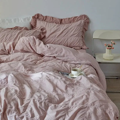 Pink bedding with a cup and saucer on a bed in a bedroom setting.