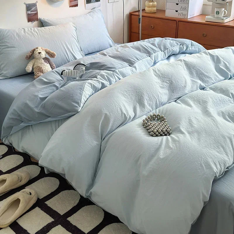 Light blue bedding set on a bed with a teddy bear and slippers in the foreground.