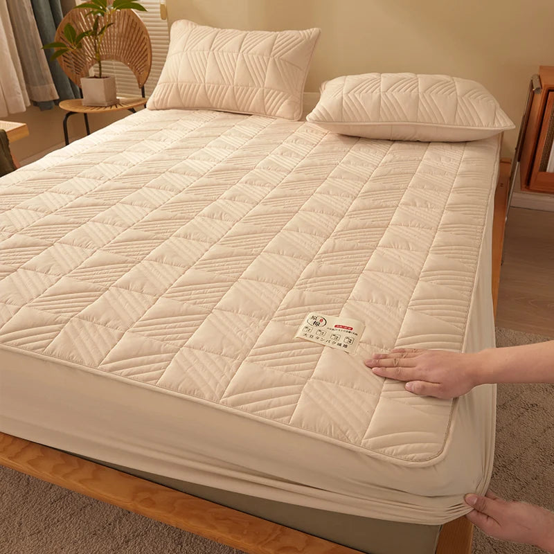 Beige quilted mattress cover on a bed with a person adjusting it, in a bedroom setting.