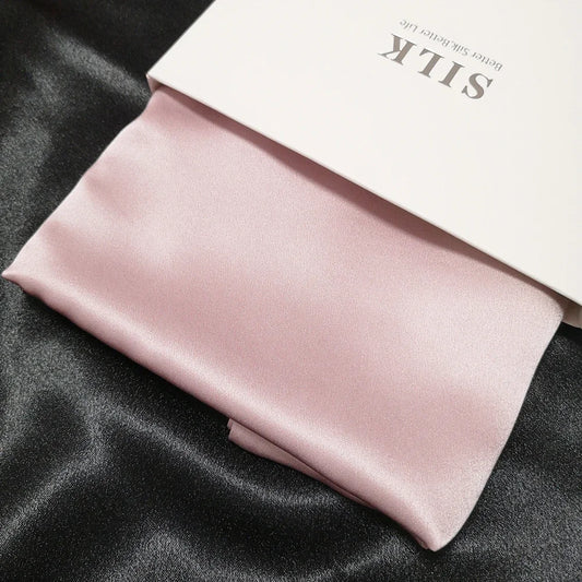Pink satin pillowcase on a black satin surface with 'SILK' branding.