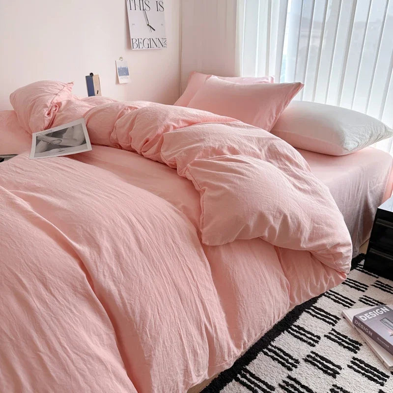 Pink bedding set on a bed with a white wall and decor in the background