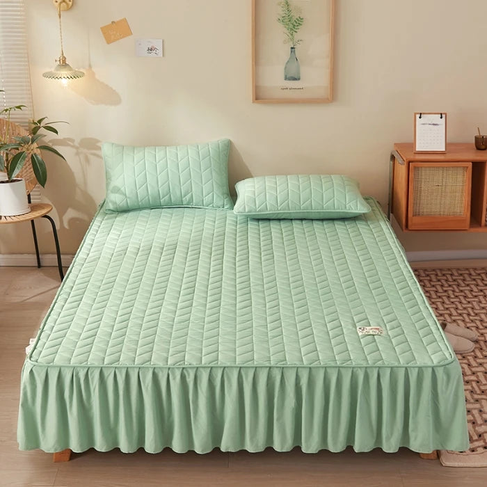 Green quilted bedspread set on a bed in a bedroom with a wooden nightstand and plant.
